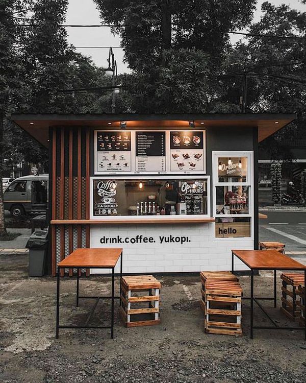 an outdoor coffee shop with tables and stools around the outside table, in front of some trees