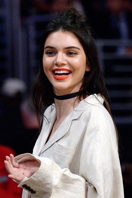 a woman wearing a white shirt and black choker smiles at the camera while standing in front of a red car