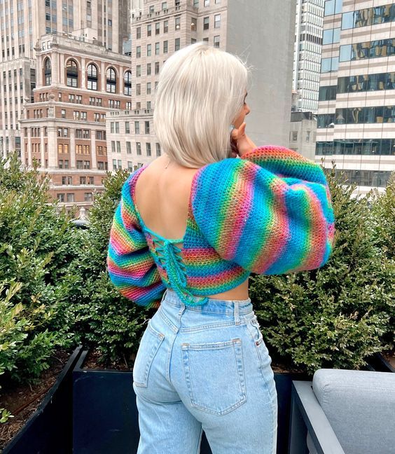 a woman with blonde hair wearing blue jeans and a rainbow striped sweater looking over her shoulder