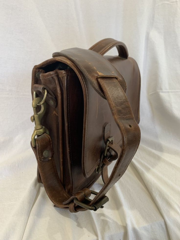 a brown leather bag sitting on top of a white sheet