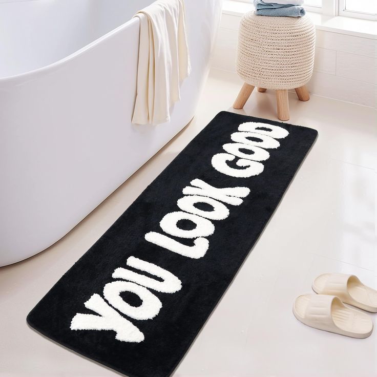 a black rug that says go goa on it next to a bathtub and slippers