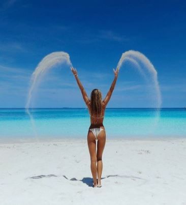 a woman standing on top of a sandy beach next to the ocean with her arms in the air