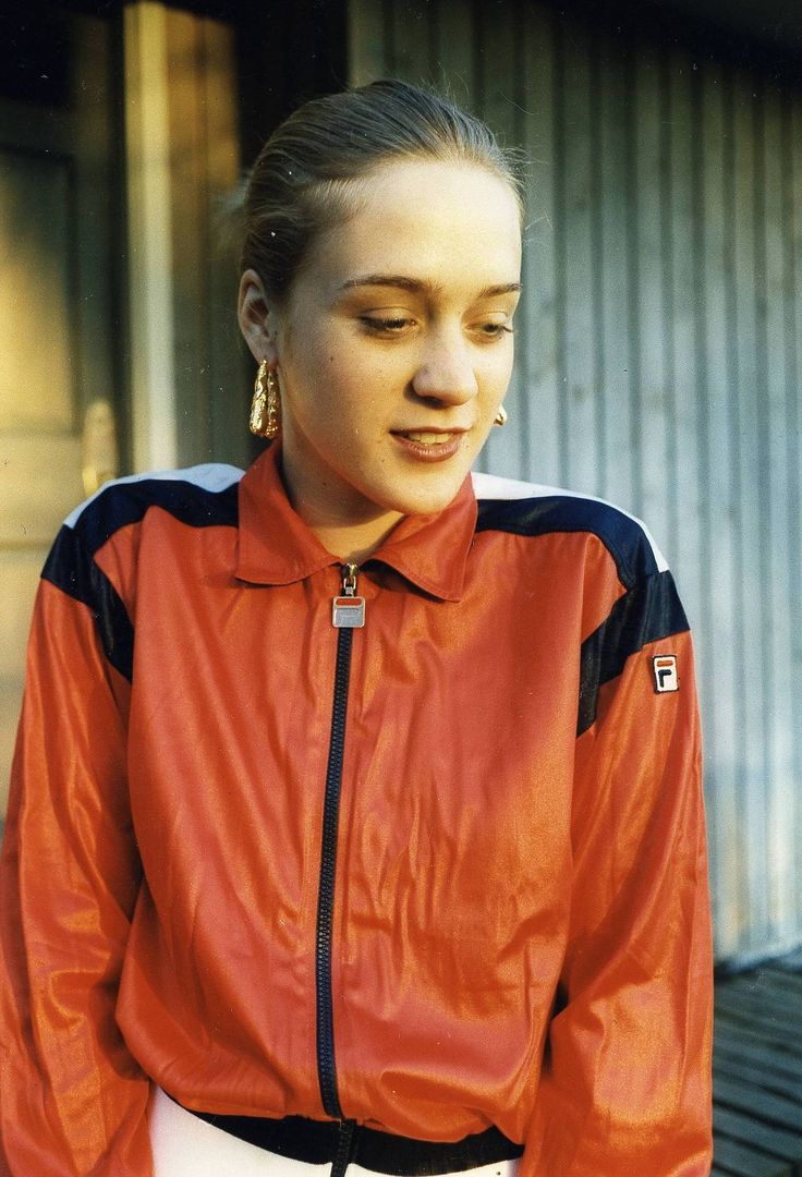 a woman wearing a red jacket and black pants standing in front of a garage door