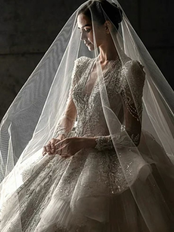 a woman in a wedding dress with a veil over her head and hands on her chest