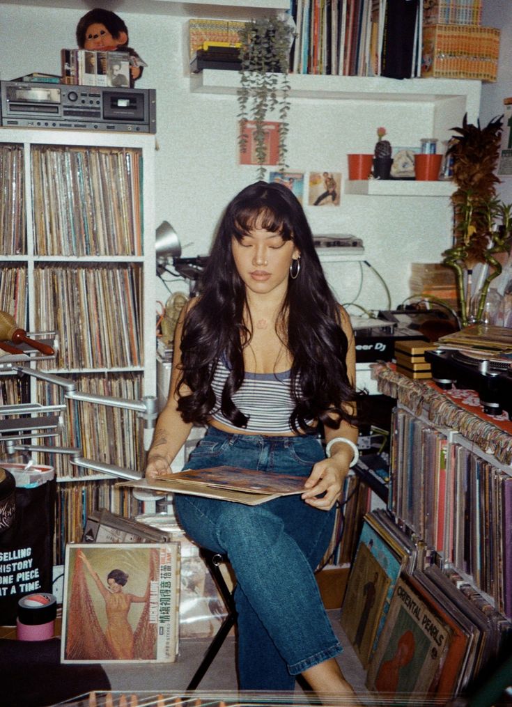 a woman sitting on a chair in front of a record shelf filled with vinyl records