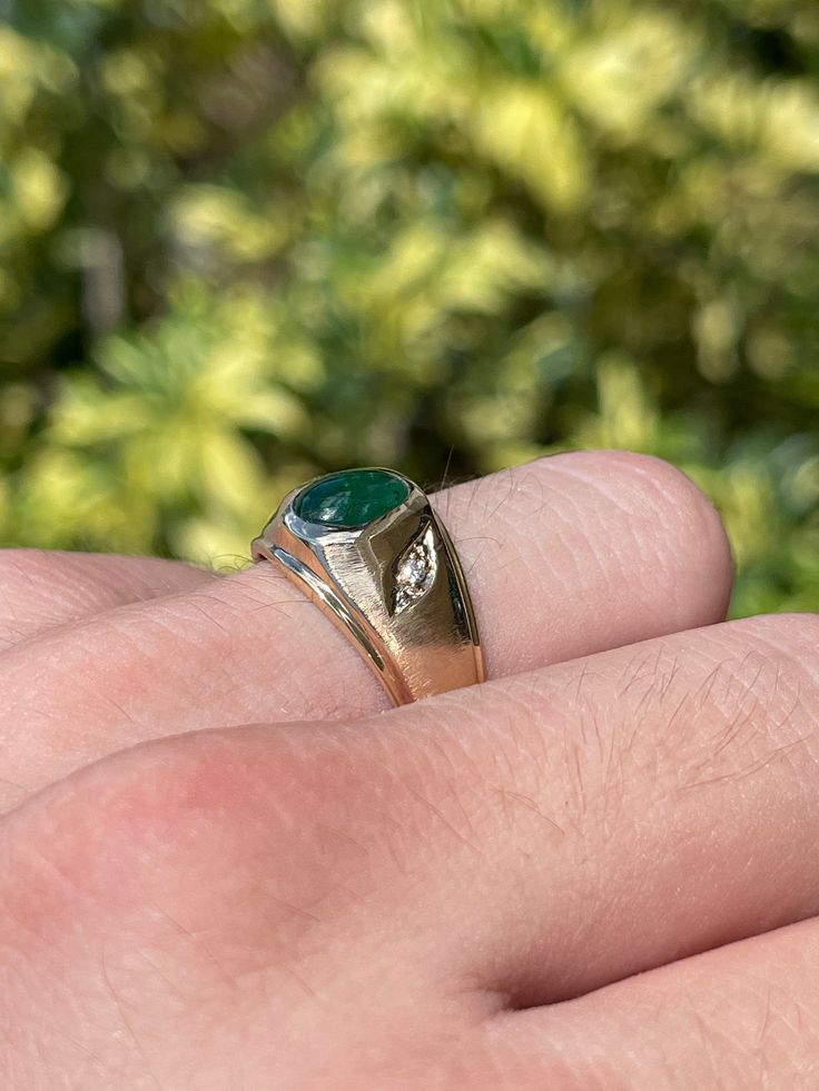 A beautiful three-stone, natural emerald cabochon, and diamond ring. The center stone cabochon has a full 1.36-carats, with a dark green color and very good luster. Accenting the cabochon are two petite brilliant round diamonds. This one-of-a-kind ring is in 10K yellow gold, with a satin finish going halfway down the band giving it the perfect touch. Setting Style: Three-Stone Setting Material: 10K Yellow Gold Gold Weight: 5.8 Grams Main Stone: Emerald Cabochon Shape: Oval Cut Weight: 1.36-Carat Classic Signet Ring With May Birthstone, Oval Gemstones With Bezel Setting For Anniversary, Classic Signet Ring With Polished Finish For May Birthstone, Anniversary Signet Ring With May Birthstone, Green Round Signet Ring With Prong Setting, Classic Marquise May Birthstone Jewelry, Classic Marquise Jewelry For May Birthstone, Oval May Birthstone Jewelry With Polished Finish, Classic Cabochon Emerald Ring For Formal Occasions