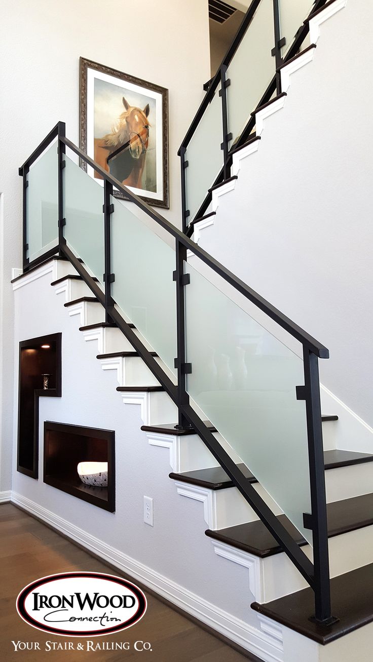 a staircase with glass railing and black handrails next to a fire place on the wall