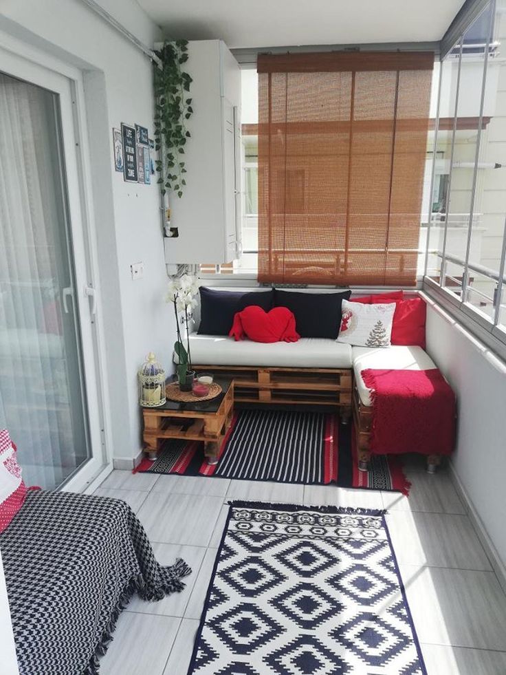 a small balcony with black and white rugs, red pillows, and wooden pallets