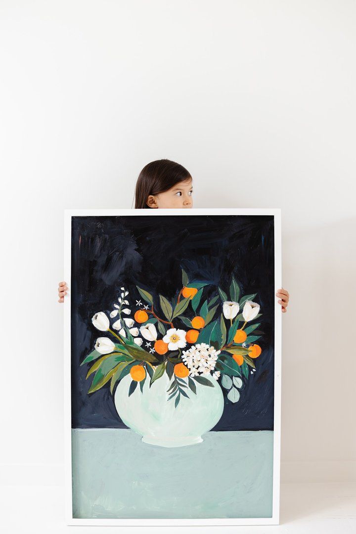 a woman holding up a painting with flowers in it's white vase on a black background