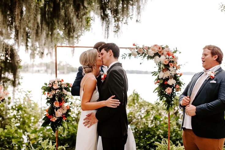 a bride and groom kiss as they stand under an arch decorated with flowers