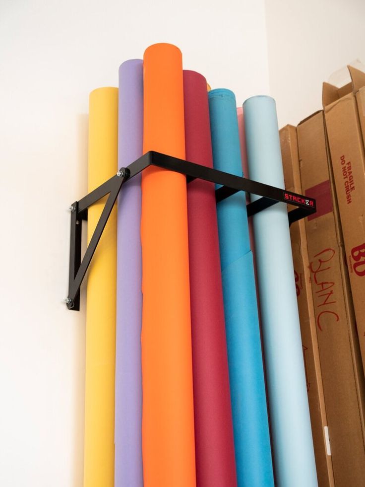 a bunch of different colored yoga mats hanging on a wall next to cardboard boxes and a pair of scissors