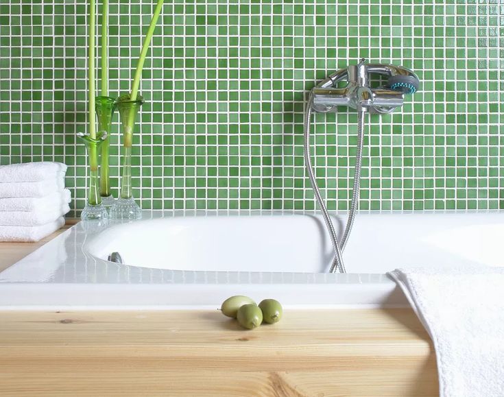 a bathroom with green tile and white bathtub next to bamboo stalks on the counter