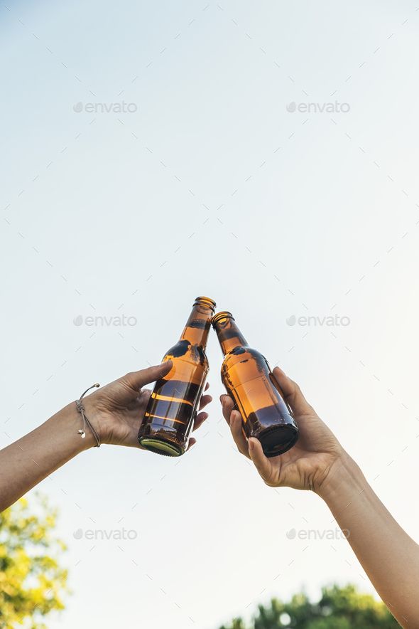 two people holding beer bottles up in the air - stock photo - images and pictures