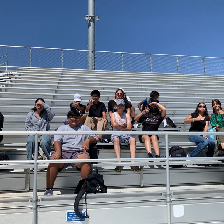 some people sitting on bleachers and one is holding a cell phone