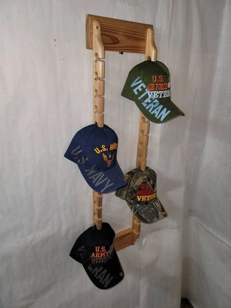 three hats are hanging from a wooden rack on a white sheeted wall, and one hat is in the shape of a ladder