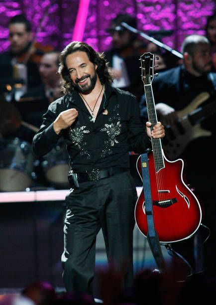 a man holding a red guitar in front of a microphone and other people behind him