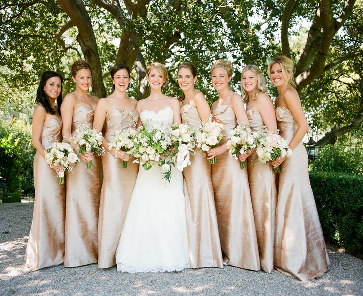 a group of women standing next to each other in front of a tree and bushes