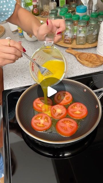 a woman cooking tomatoes in a frying pan on top of a stove with an orange liquid