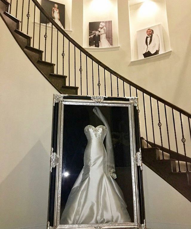 a white wedding dress in a box on the ground next to a stair case with pictures above it