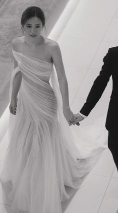 a man and woman in formal wear holding hands while walking down a hall with white tiles on the floor