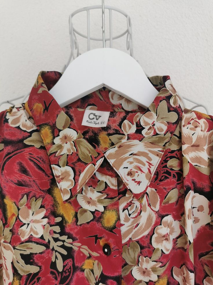 Vintage floral print polyester blouse from the 1980's. Women's button down floral print blouse in red, green, beige and yellow colors. Has elastic bottom hem and a pleated detail on the shoulders (with shoulder pads). Oversized fit. Material: 100% Polyester Size: 44 DE which is 14 US or XL. Model on the picture is 40 DE. To be sure this item would fit you, please look at the measurements below. Measurements (taken while blouse is lying flat, double waist): Shoulder to Shoulder (from seam to seam Red Floral Print Retro Shirt, Red Retro Floral Print Shirt, Retro Red Floral Print Shirt, Red Vintage Print Shirt, Red Vintage Shirt With Vintage Print, Vintage Red Shirt With Floral Print, Red Collared Printed Blouse, Vintage Red Shirt For Spring, Red Printed Collared Blouse