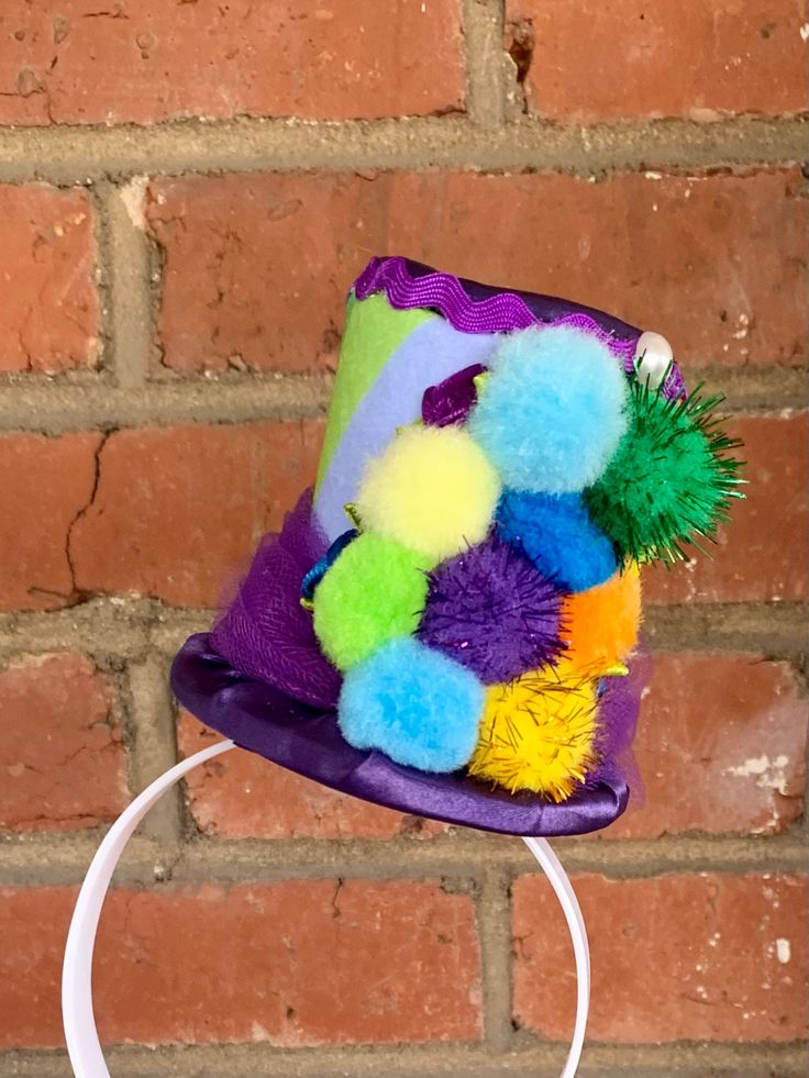 This whimsical mini top hat is made of foam and layers of cardstock covered with purple satin on the top & bottom, and patterned felt in rainbow colors in the middle. It is then trimmed with ribbon, tulle, and other accents, all in bright colors. A white plastic headband is glued to the hat so it will tilt slightly to the left side of your head. This hat is ready to ship! --------------------------------------------------------------------------------------------------------------------------------- Approximate measurements: Height of hat = 3.5 inches Brim of hat = 3.5 x 4 inches --------------------------------------------------------------------------------------------------------------------------------- Thank you for looking! :) You can review my Shop Policies here: http://www.etsy.com Fun Hats For Birthday And Carnival, Fun Adjustable Costume Accessories For Birthday, Fun Carnival Birthday Hats, Fun Birthday Carnival Hats, Whimsical Party Supplies For Birthday And Carnival, Adjustable Themed Top Hat For Party, Adjustable Themed Costume Accessories For Birthday, Playful Hats For Birthday And Carnival, Playful Party Hat Costume Accessories