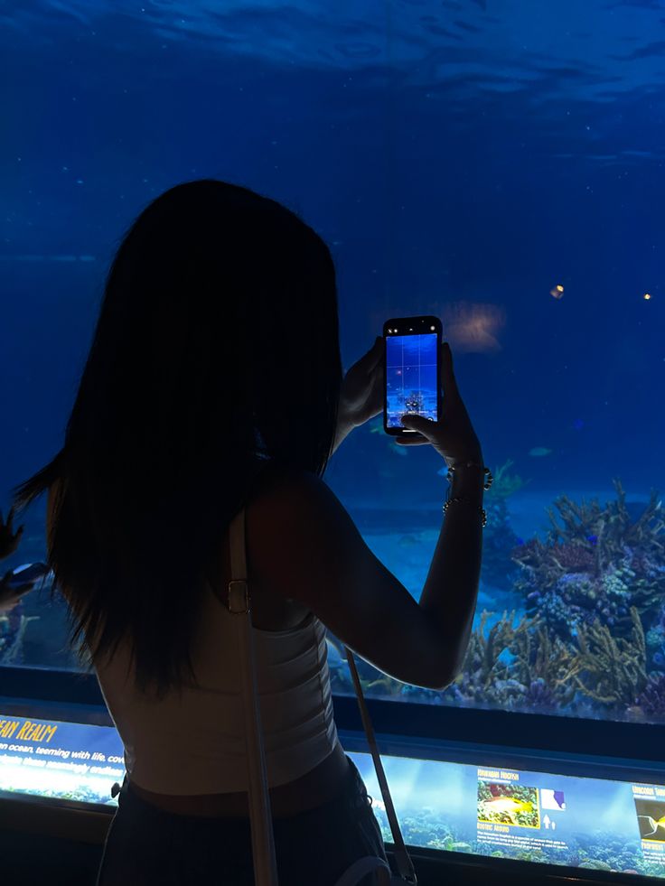 a woman taking a photo in front of an aquarium with her cell phone at night