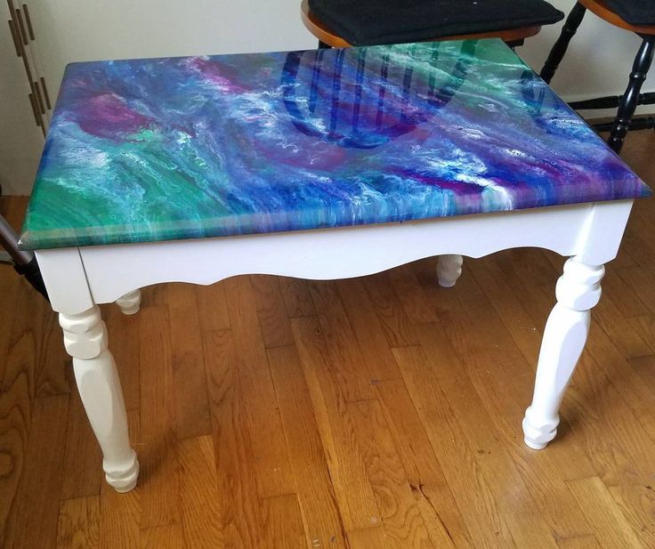 a white table with colorful paint on it and two stools in the back ground