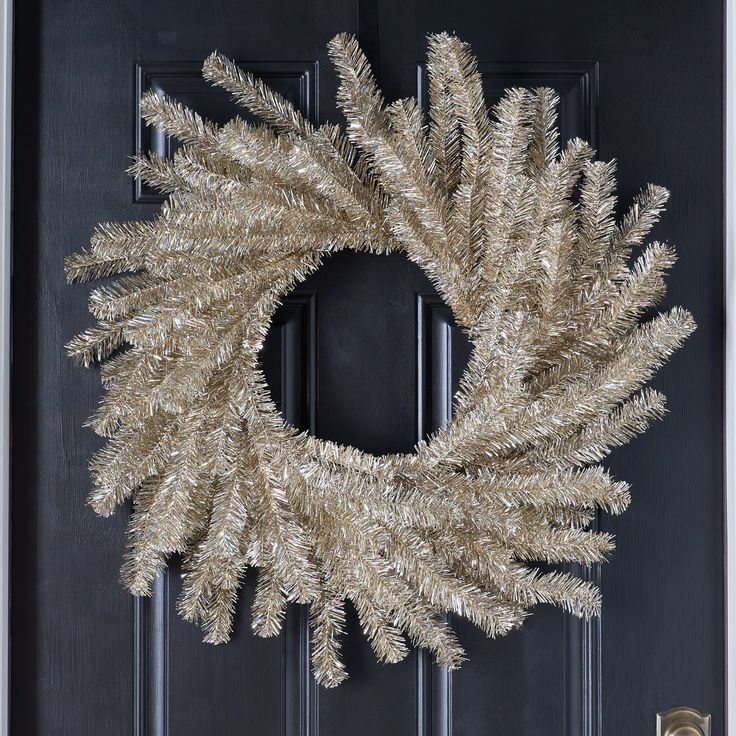 a christmas wreath on the front door of a house with gold tinsel and black trim