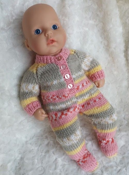 a baby doll with blue eyes laying on a white blanket wearing a sweater and pants