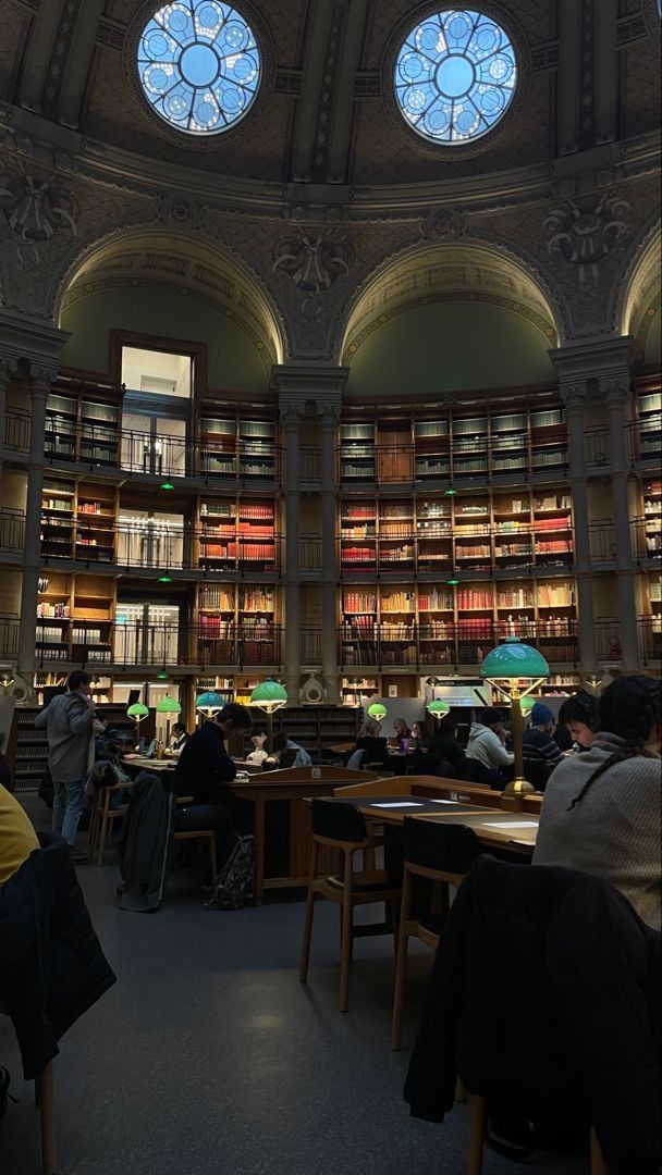 people are sitting at tables in the library with many bookshelves full of books