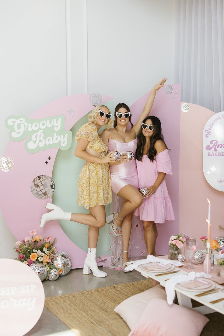 three women in pink dresses posing for the camera at a baby shower party with balloons and decorations