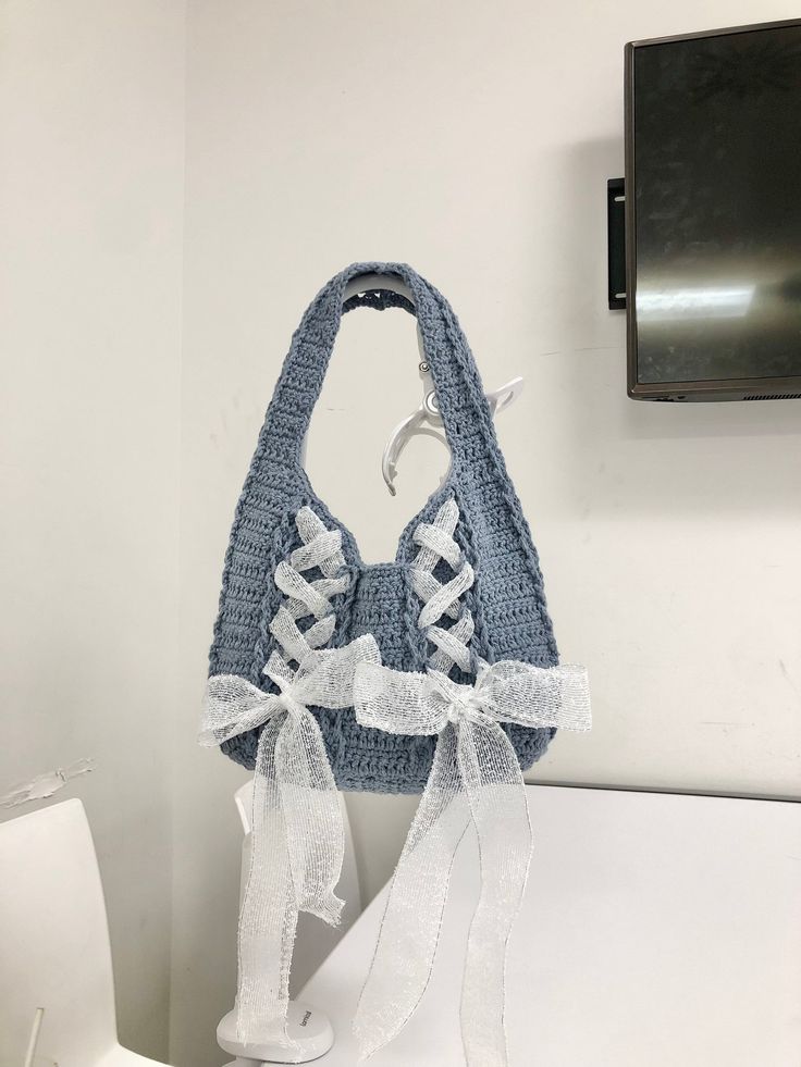 a crocheted purse hanging on the wall next to a toilet with a white ribbon tied around it