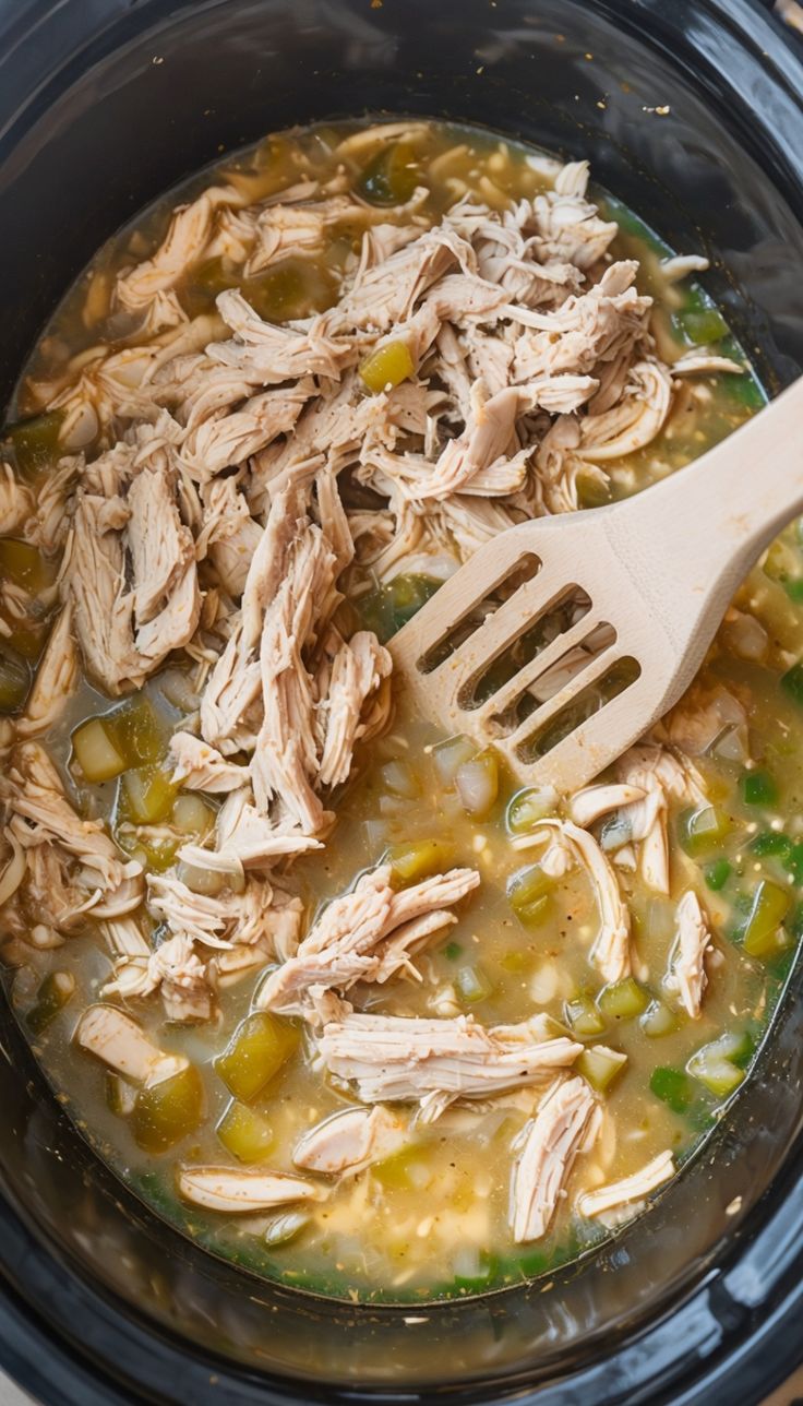 a crock pot filled with chicken and vegetables next to a wooden spoon in it