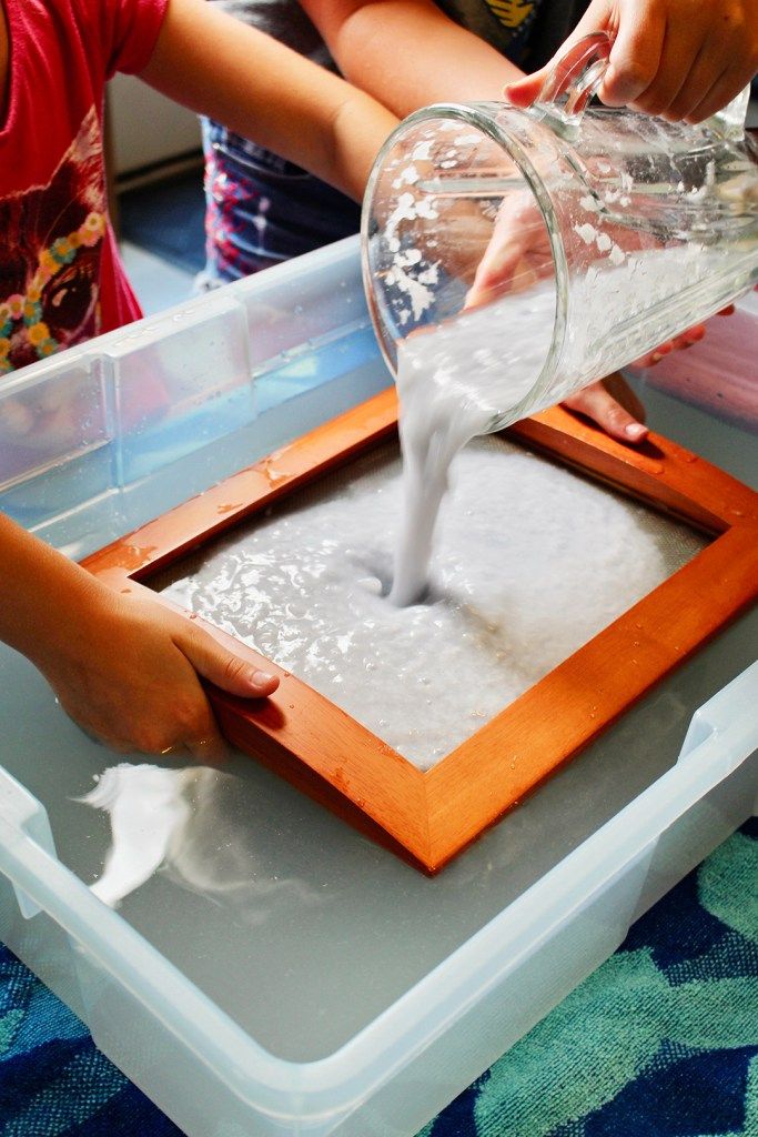 a child pouring milk into a container on top of a tray with other children in the background