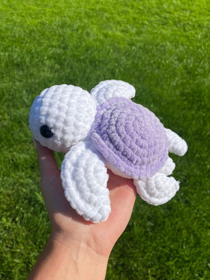 a small crocheted turtle is held in someone's hand on the grass