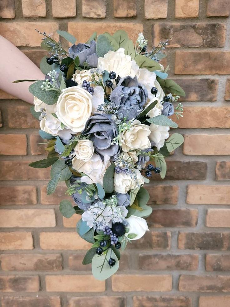 a bridal bouquet with blue and white flowers on a brick wall in front of a woman's hand