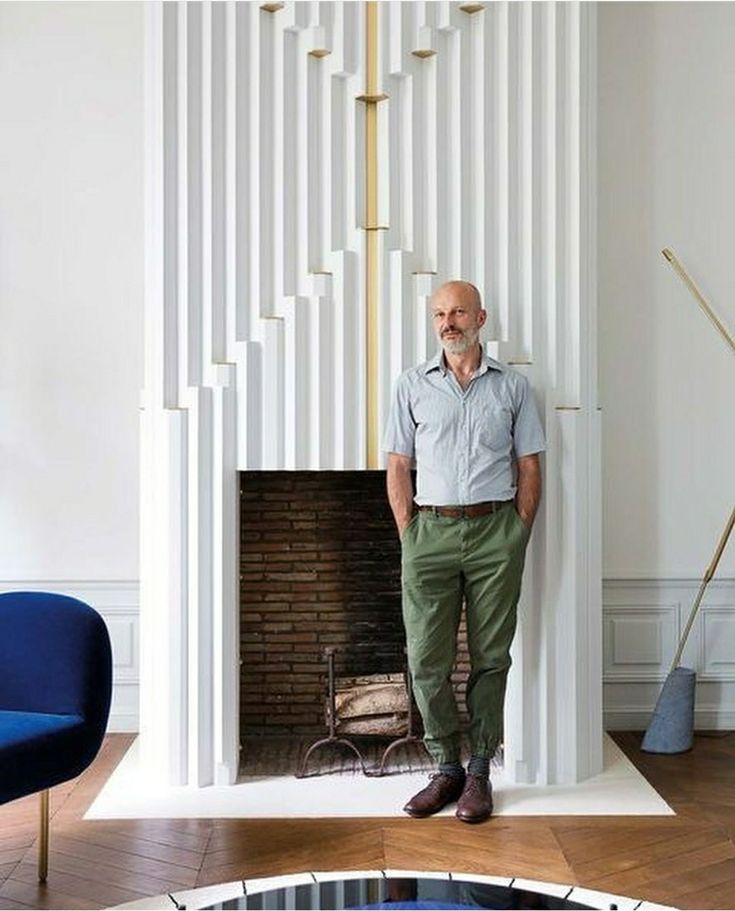 a man standing next to a fireplace in a room with white walls and wooden floors