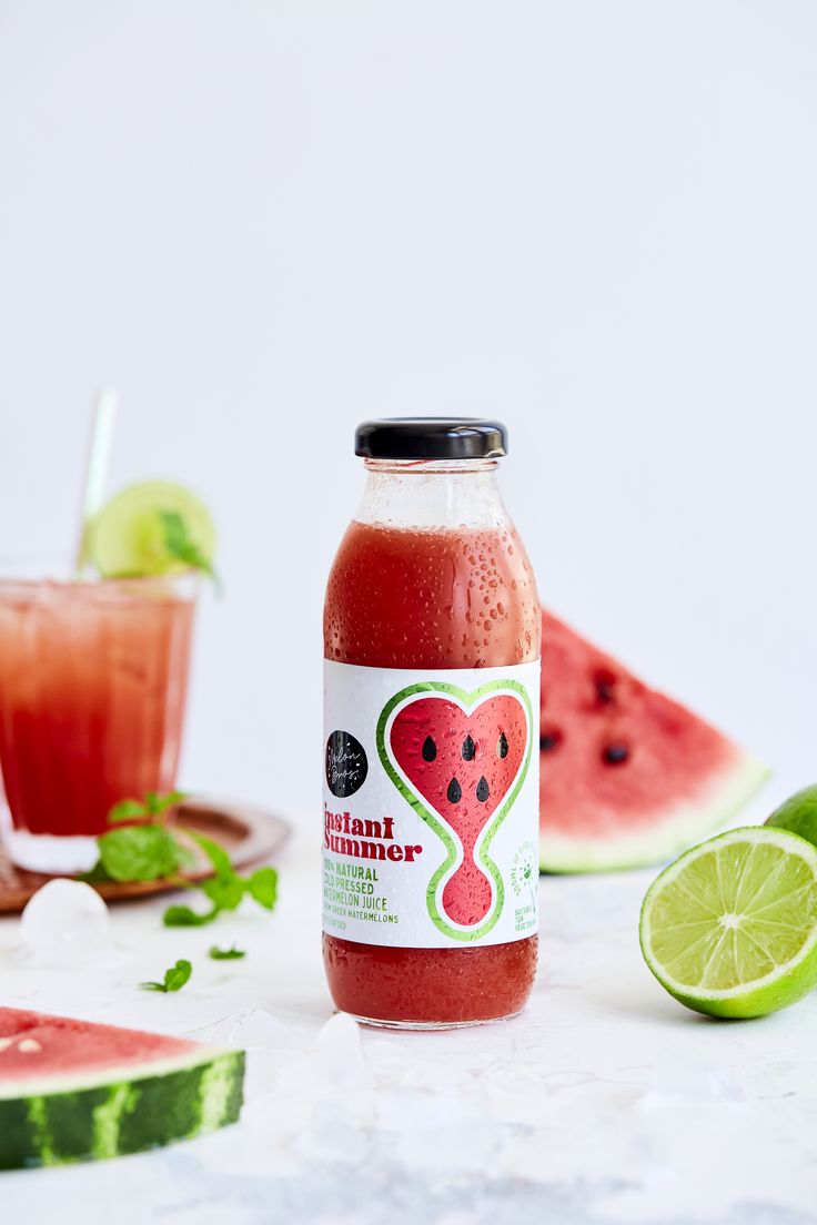 a bottle of watermelon juice next to slices of watermelon and lime