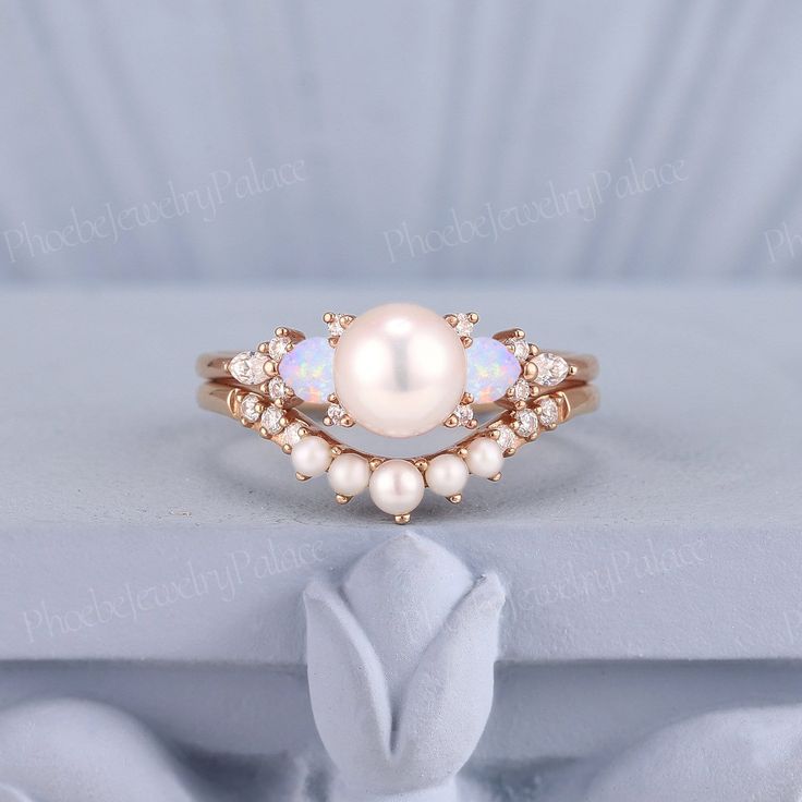 a white pearl and diamond ring sitting on top of a piece of cloth in front of a