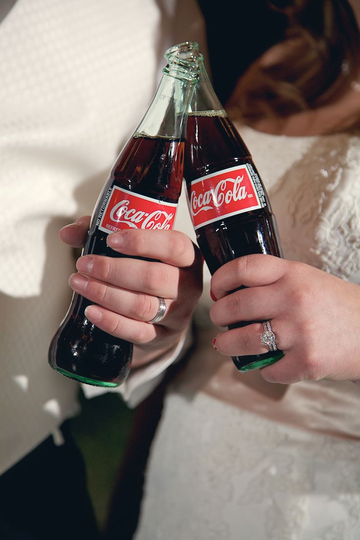 the bride and groom are holding two coca - cola bottles in their hands, both wearing wedding rings