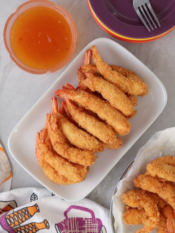 some fried food is on a white plate next to orange juice and silverware,