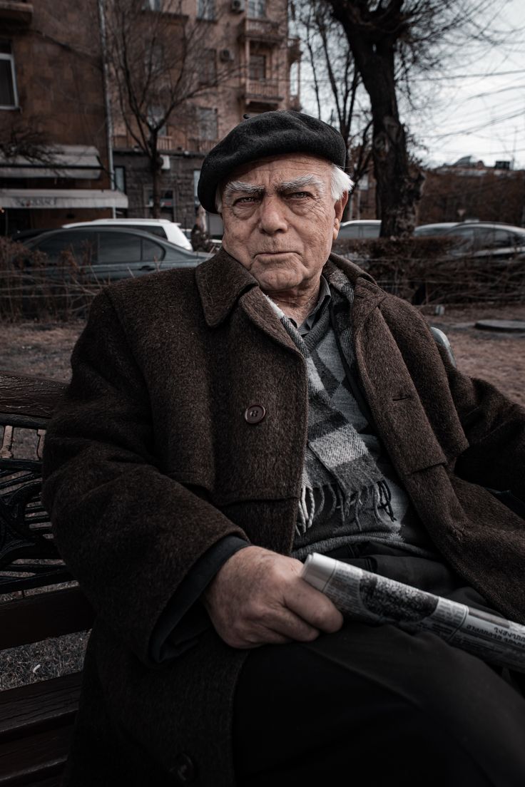 an old man sitting on a bench with a baseball bat in his hand and looking at the camera