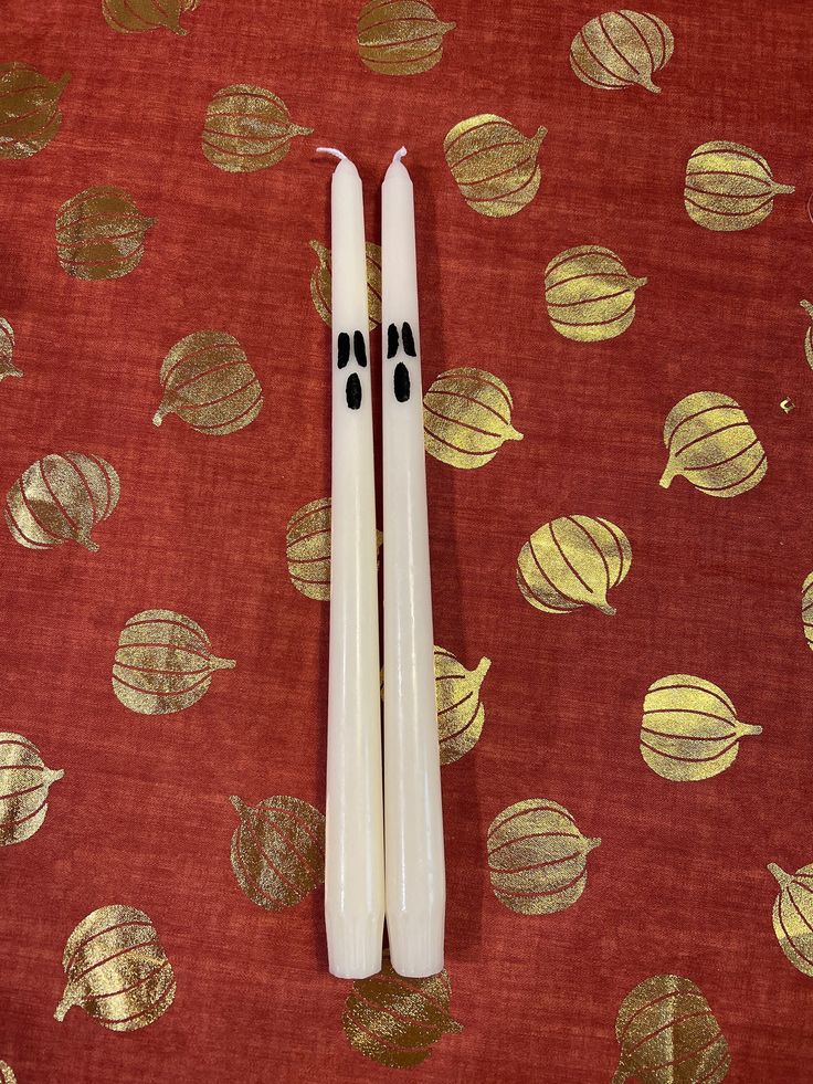 two white candles sitting on top of a red table cloth