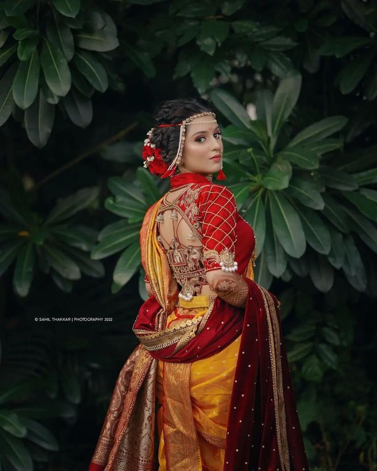 a woman in a red and yellow dress standing next to some trees with green leaves