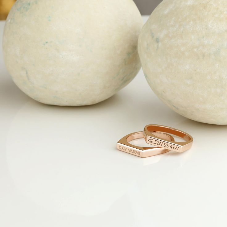 two gold wedding bands sitting on top of a white table next to an orange ball