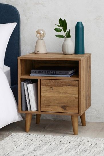 a nightstand with two books on it next to a blue headboard and white sheets