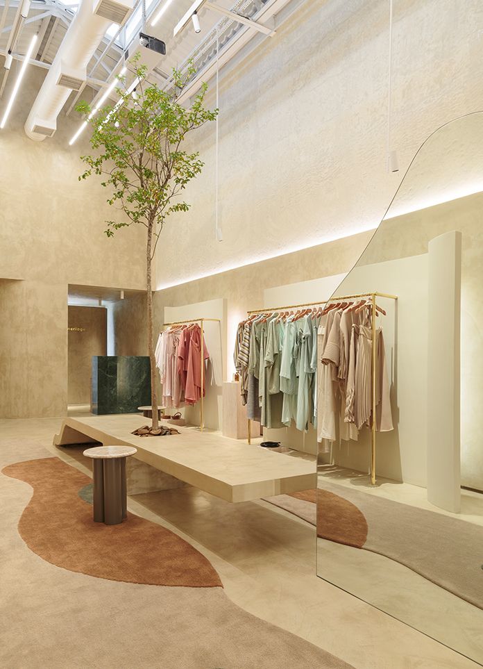 an empty clothing store with clothes on racks and trees in the center, as well as mirrors