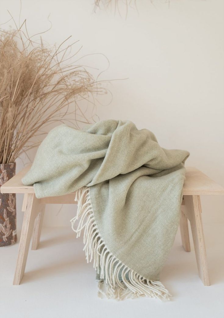 a blanket sitting on top of a wooden bench next to dried plants and vases