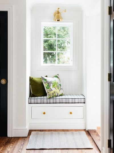 a window seat with pillows on it in front of a white wall and wooden floor